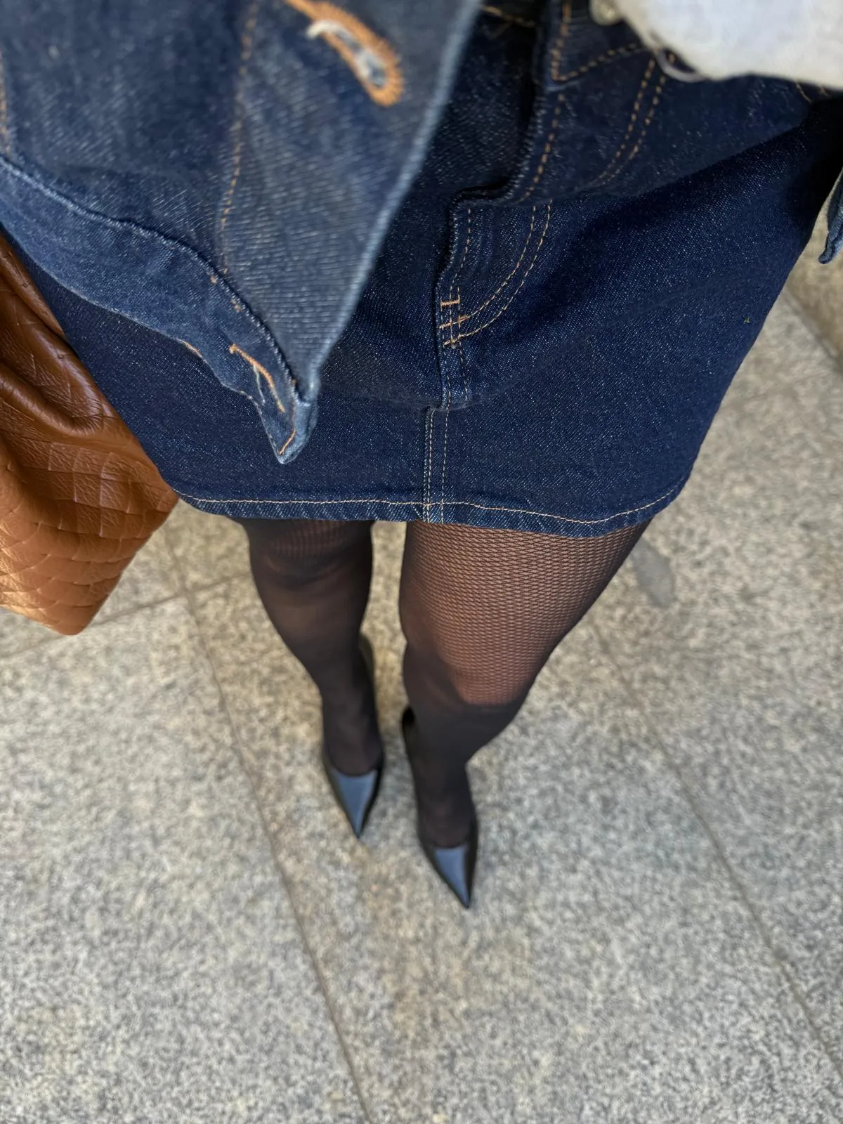 Jak Nosić Rajstopy? Kompletny Przewodnik Stylistki Stylizacja z rajstopami kabaretkami widziana z góry: kobieta ma na sobie jeansową spódnicę mini, czarne szpilki w szpic i trzyma brązową, skórzaną torebkę.